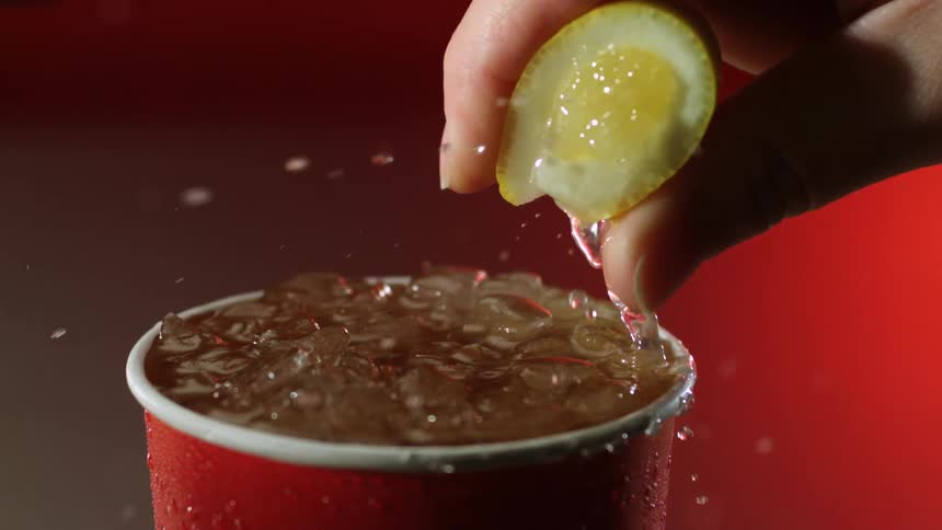 A person is squeezing a lemon on top of a beverage