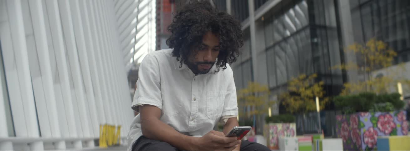 A man sits looking at his cell phone in the city