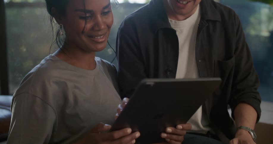 Happy young couple sitting on the living room floor laughing while using a tablet