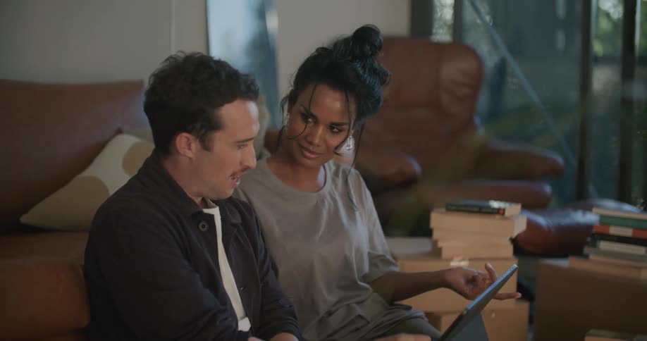 A man and a woman are sitting on a couch looking at a laptop screen and talking