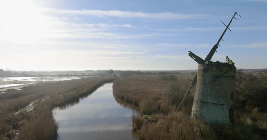 Aerial view of an abandoned windmill on the banks of a river in the countryside at morning