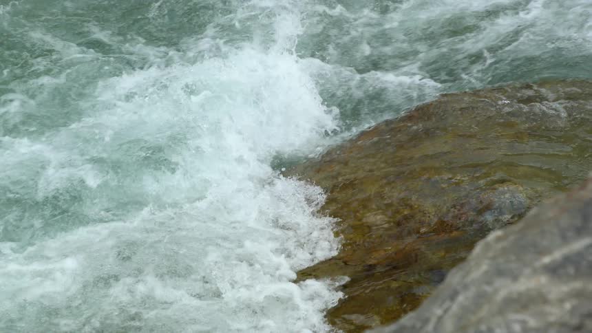 Slow motion footage of the turbulent surface of a river flowing over the rocks at daytime