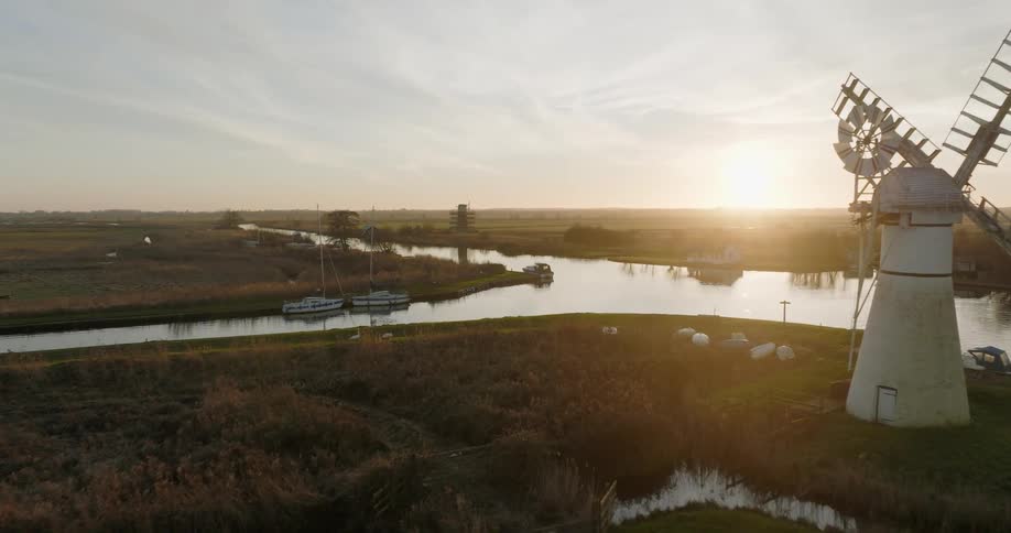 Aerial view of a white windmill on the banks of a river in the countryside at morning