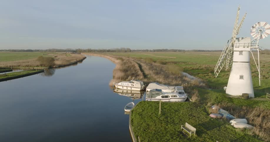 Aerial view of a white windmill on the banks of a river in the countryside at morning