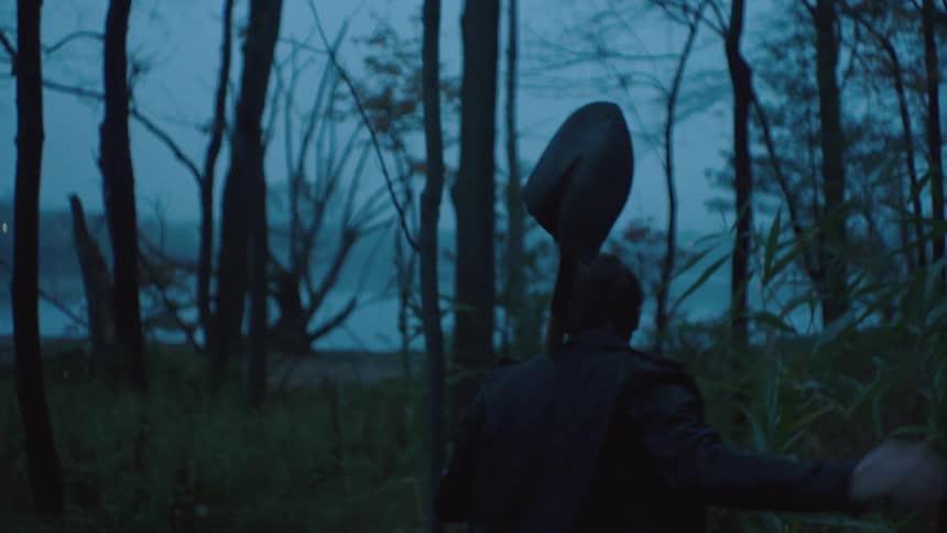 A man is carrying a shovel through the woods at sunset
