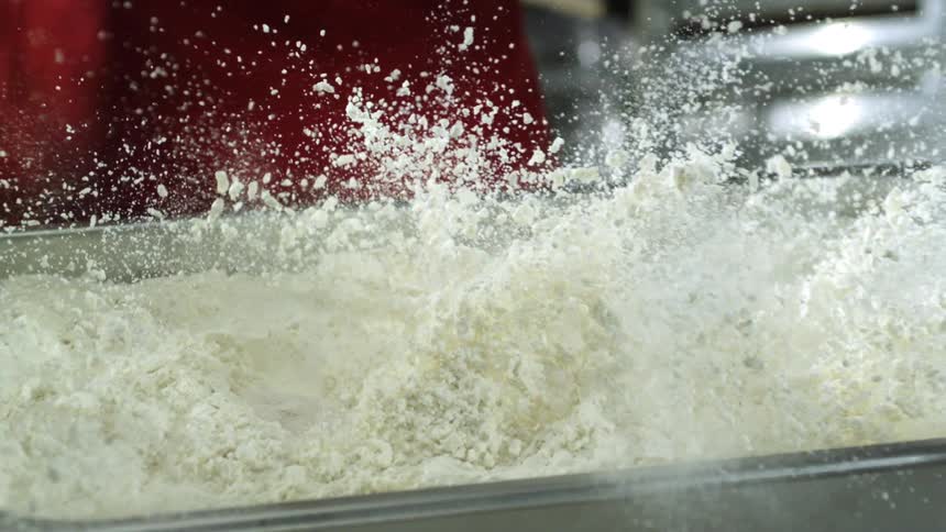 Chicken pieces drop into metaltray full of flour spraying flour about