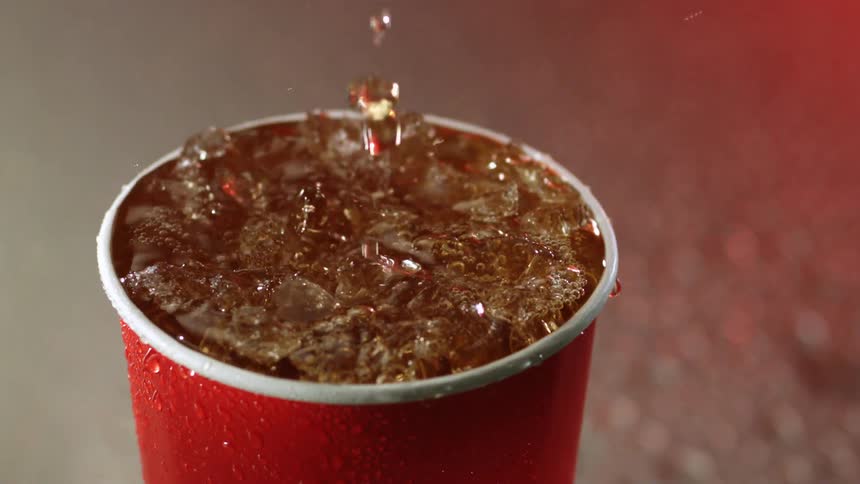 Soda pouring and splashing inside a plastic red cup filled with ice