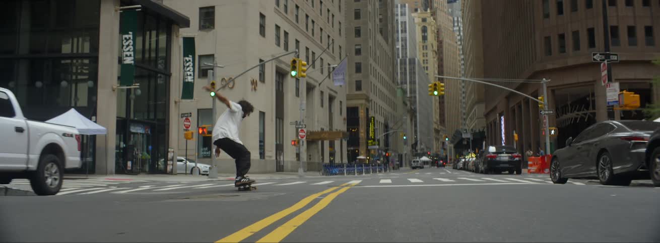 A man does tricks as he rides his skateboard on a city street