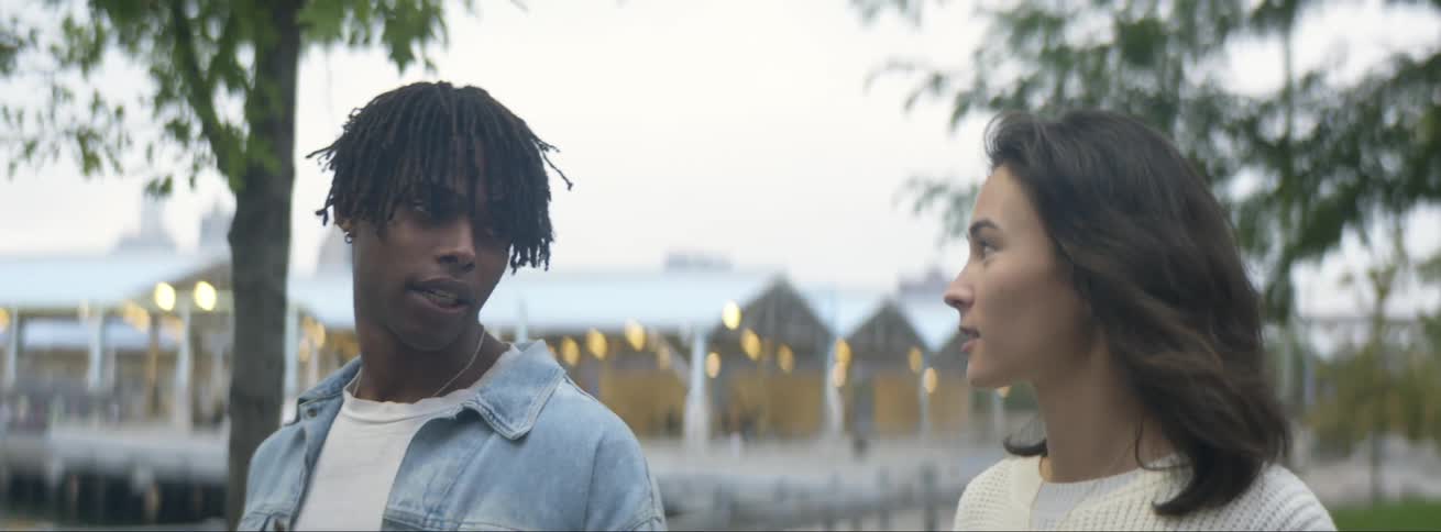 A man and woman talk as they walk side by side through a waterfront park