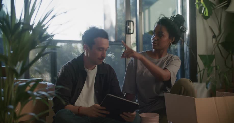A man and woman sit and talk while looking at a tablet