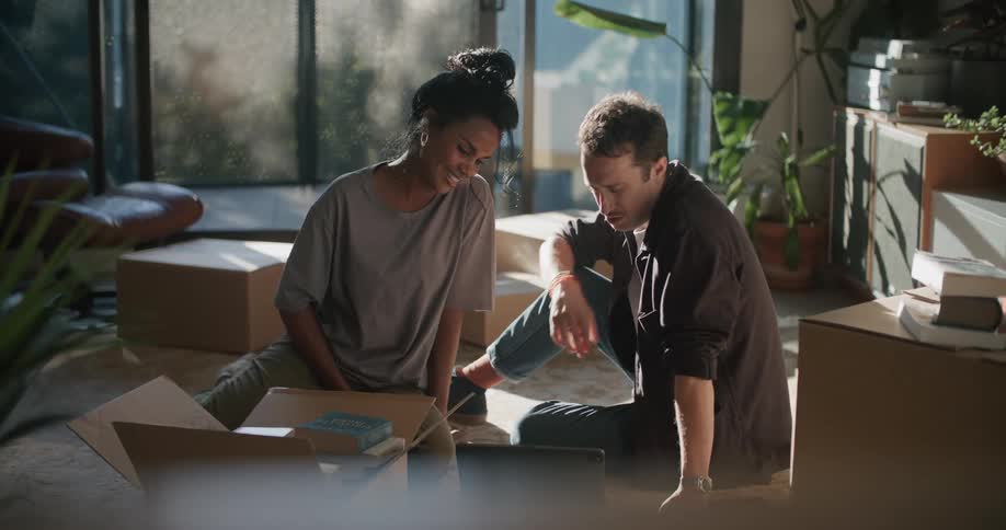 Happy young couple sitting on the living room floor laughing while using a laptop