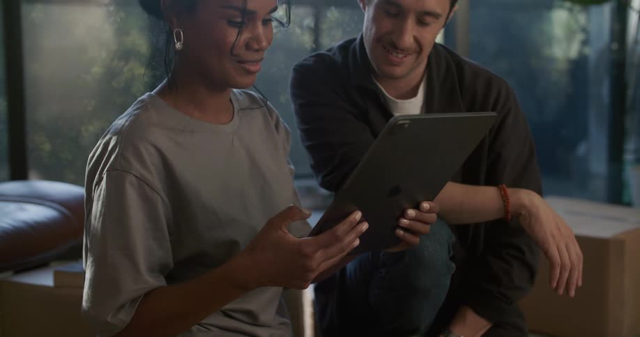 A man and woman sit around and laugh while looking at an ipad tablet