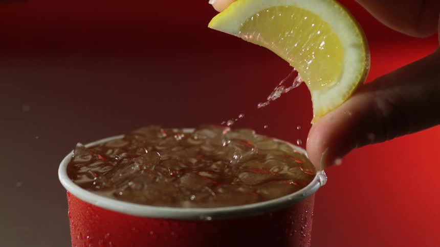 Hand squeezing a slice of lemon over a soda inside of a red plastic cup