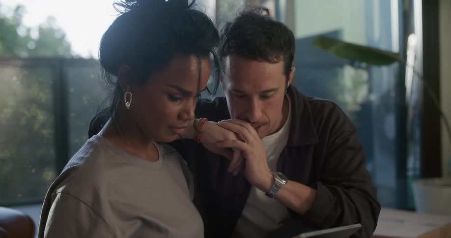 Young couple sitting in the living room surrounded by cardboard boxes checking a tablet