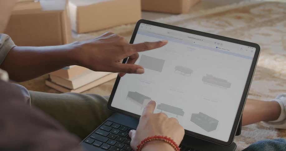 Young couple sitting on the living room floor looking at furniture online on a laptop