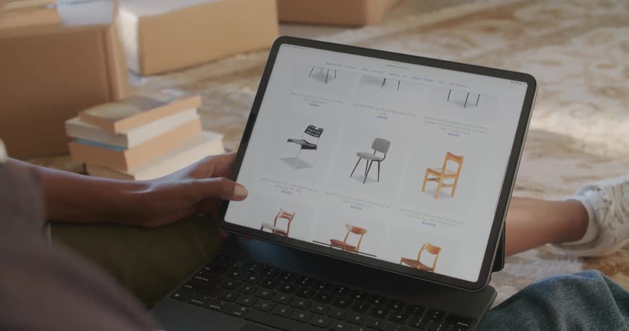 Young couple sitting on the living room floor looking at chairs online on a laptop