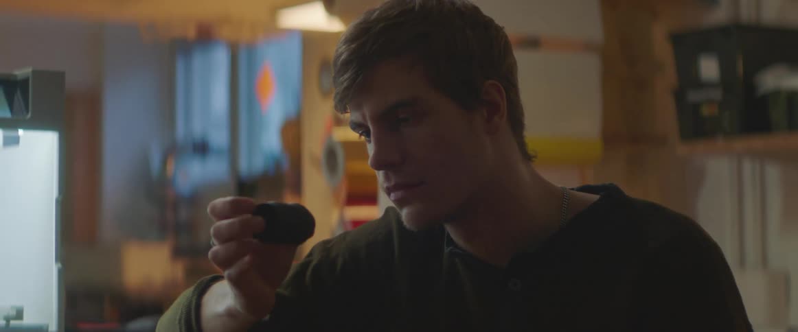 Man with black sweatshirt hold and examines object to paint with brush in lab