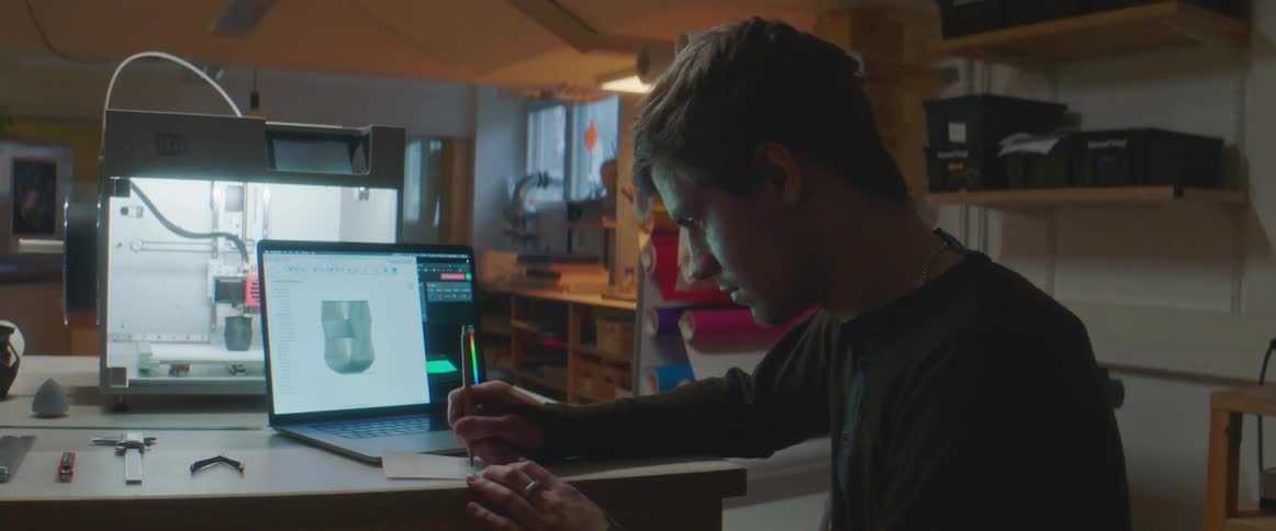 A man writing on a piece of paper in front of a computer
