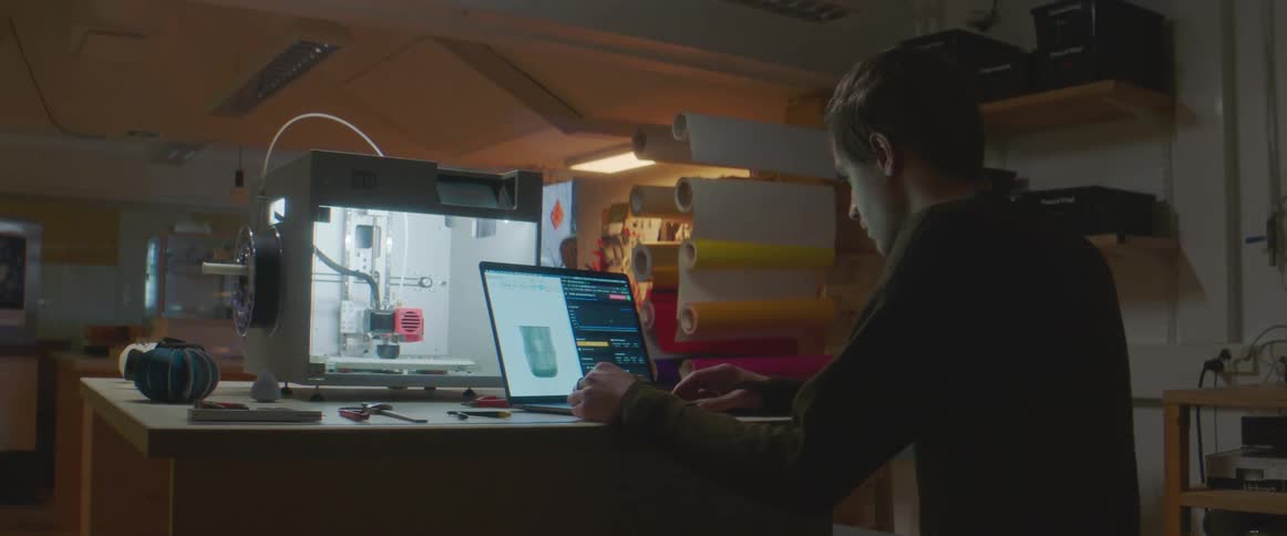 A man uses a laptop to operate a 3d printer