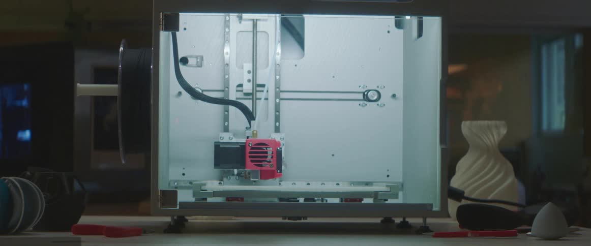 3d printer prints object on table with other objects nearby