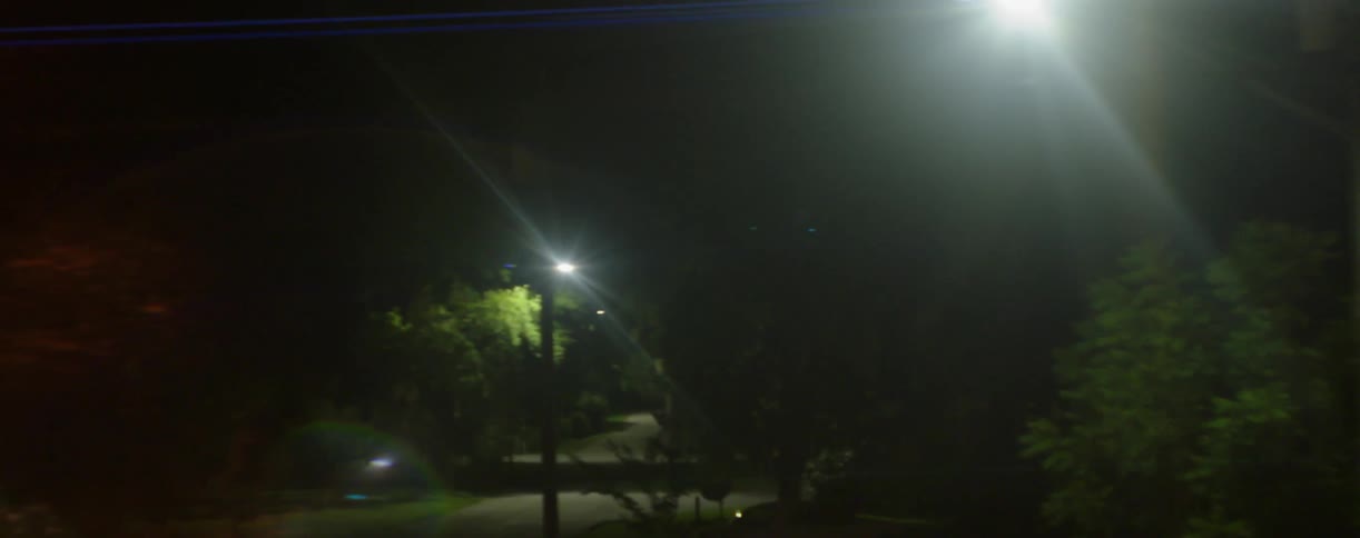 A dark neighborhood street has light posts