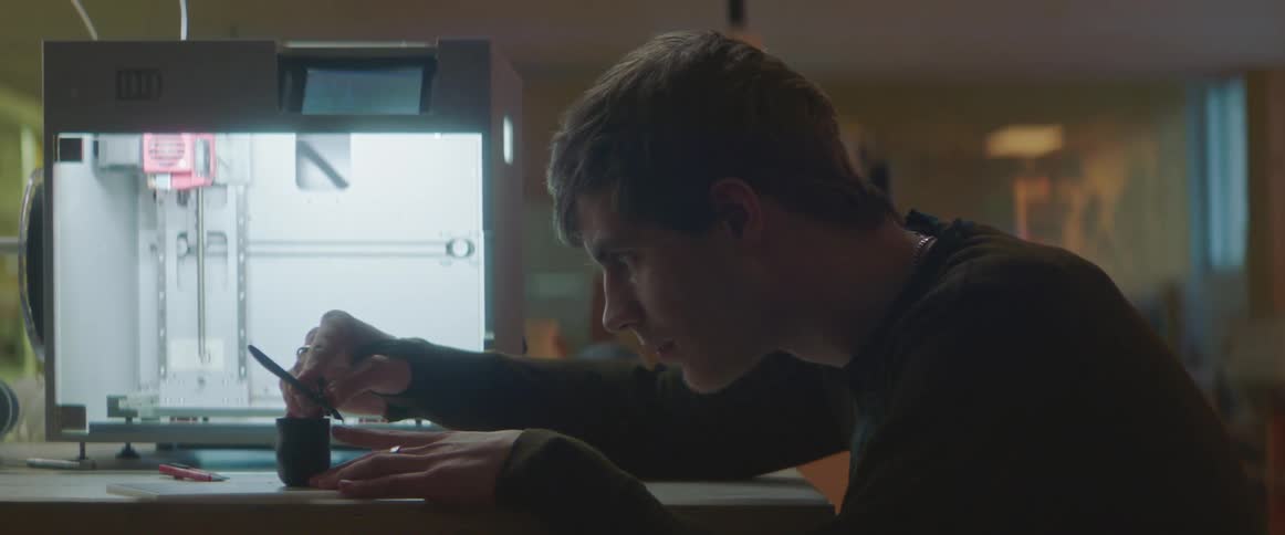 A teenager holds a blade over a small cup as he works on an experiment in a lab