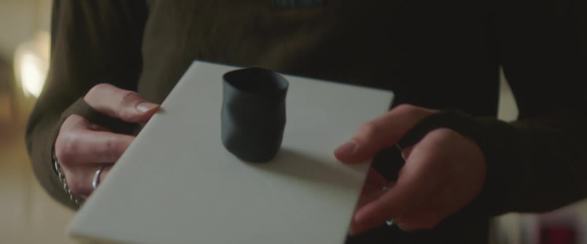 A man examines a small figurine which resembles a cup on a board and then pokes it with a pen