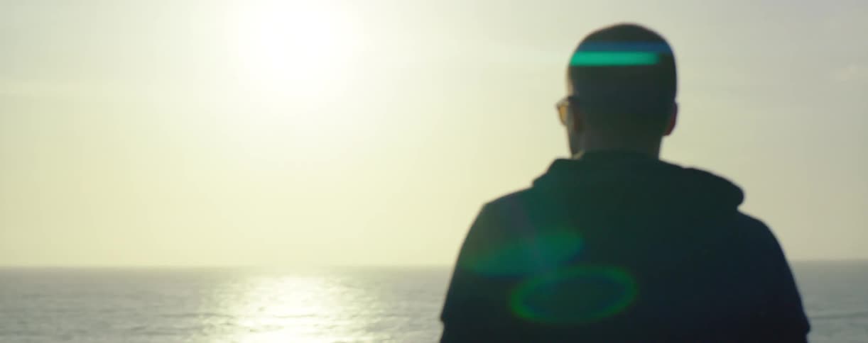 A man is watching the sun set over the water