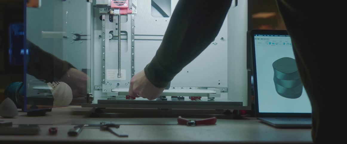 A man looks at an image on a laptop and then takes an object out of a 3d printer