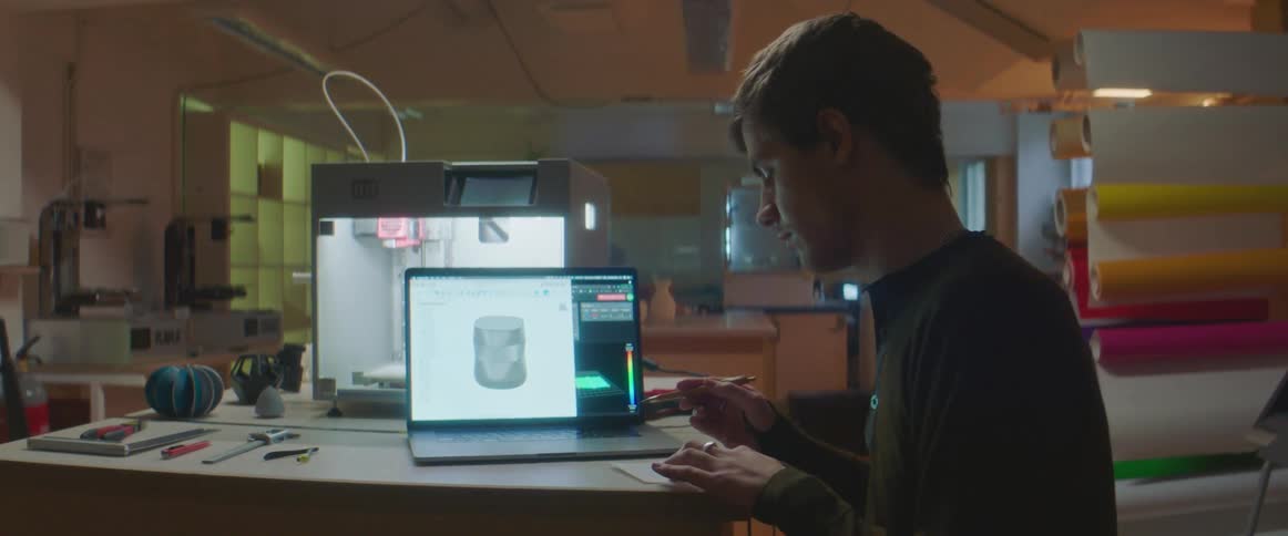 Man sits in workshop near laptop and 3d printer writing on paper