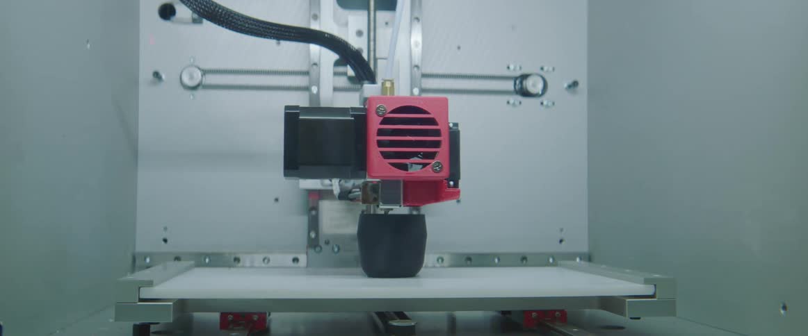 3d printer printing a vase made of black plastic inside a dimly lit warehouse