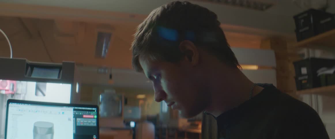 Man in black t shirt works on 3 d next to laptop in lab