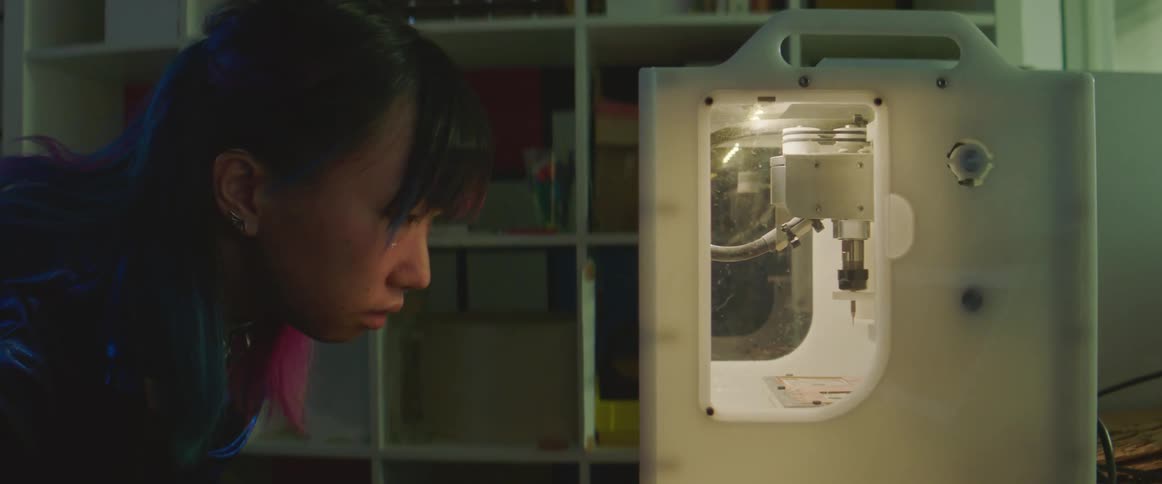Woman leans over watching machine arm moving in case