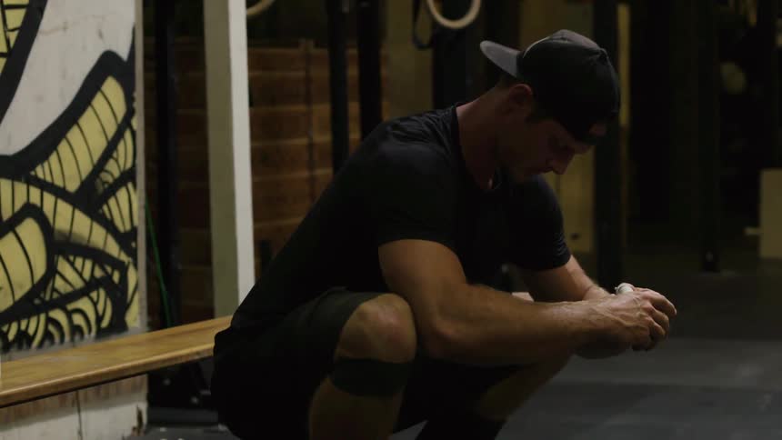 A man is crouched stretching in a gym