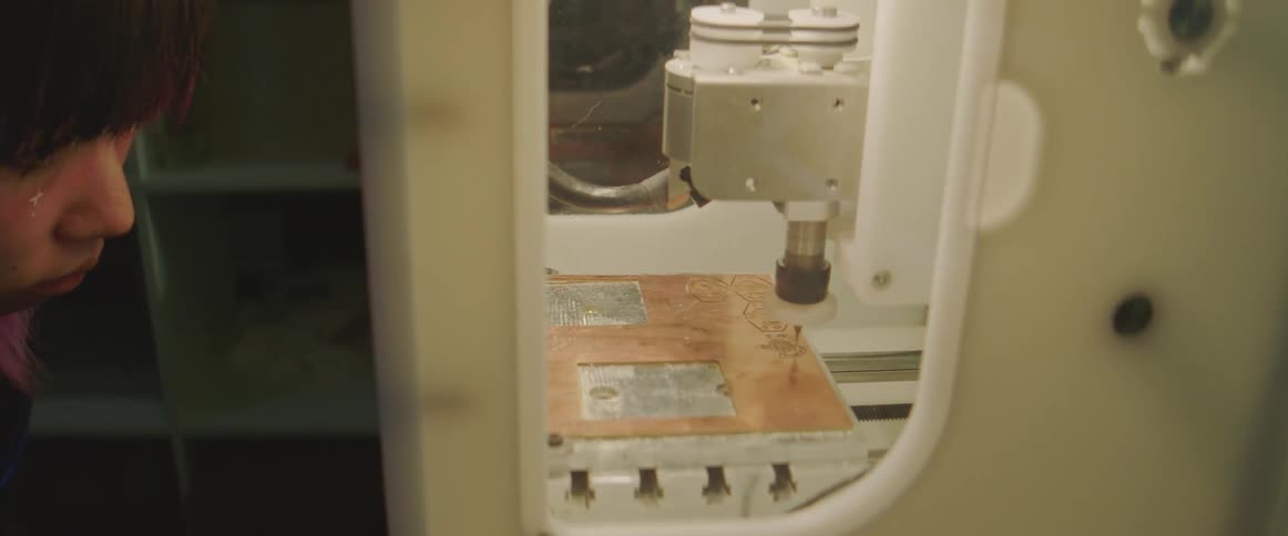 A 3d printer is working on an item while a person closely watches