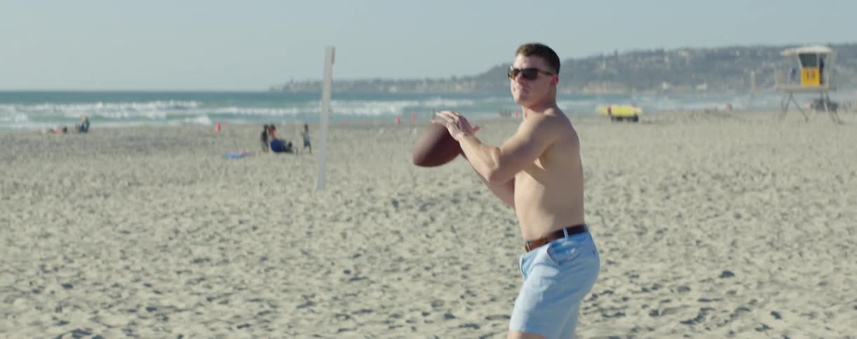 Shirtless man passes football on the beach