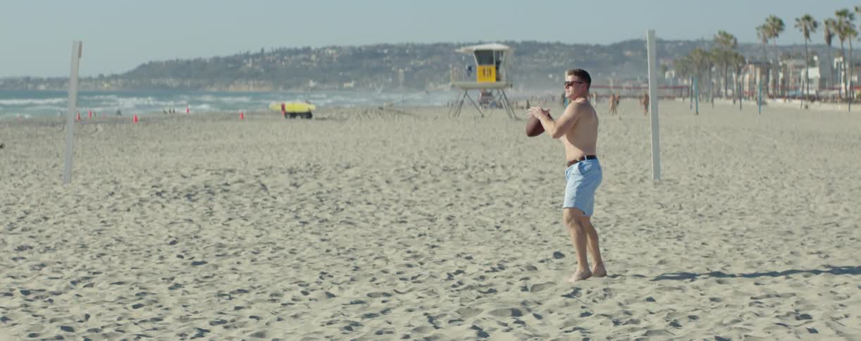 A man on the beach throws a football to a friend
