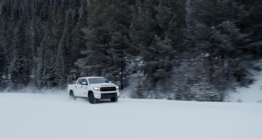 White toyota truck driving on a countryside road covered in snow near the pine tree forest in the mountain