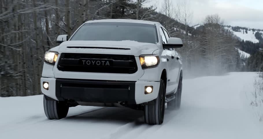 A truck travels through a wintry countryside on a road covered in snow on a cloudy day