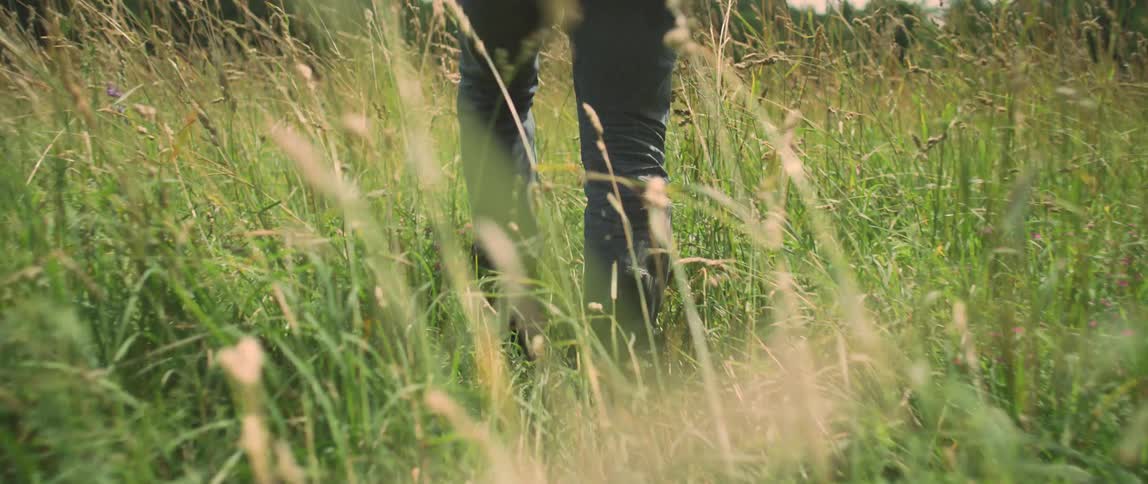 Someone wearing boots and blue jeans is walking through tall grass and weeds
