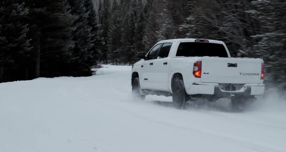 White toyota truck driving on a countryside road covered in snow near the pine tree forest in the mountain