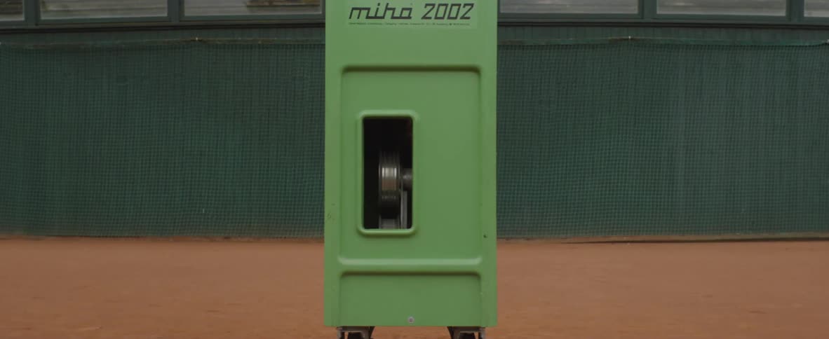 Green tennis ball machine in the middle of a tennis court at daytime