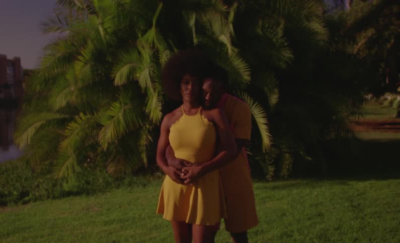 Young couple wearing yellow matching outfits hug while looking at the camera at sunset