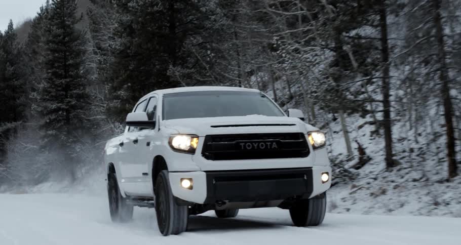 White toyota truck driving on a countryside road covered in snow near the pine tree forest in the mountain