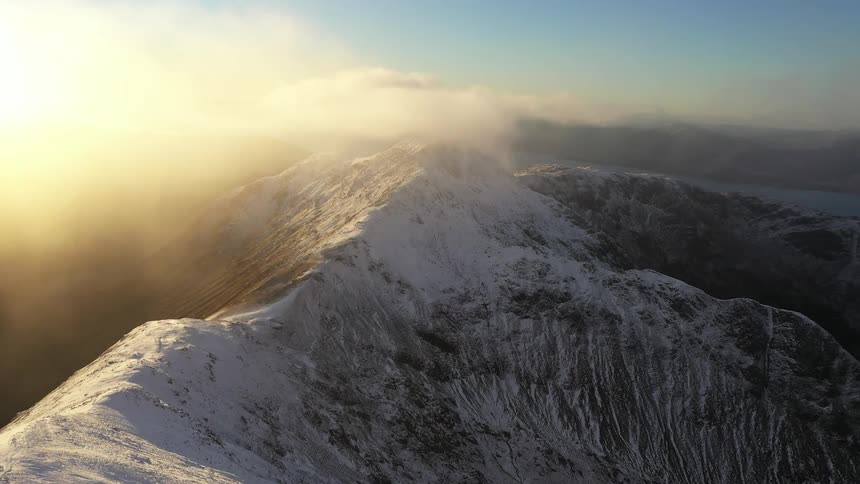 The sun shines brightly on snow covered mountains high in the clouds