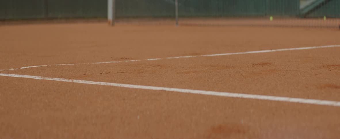 A tennis ball hits the ground near the line markings on an outdoor tennis court during the day