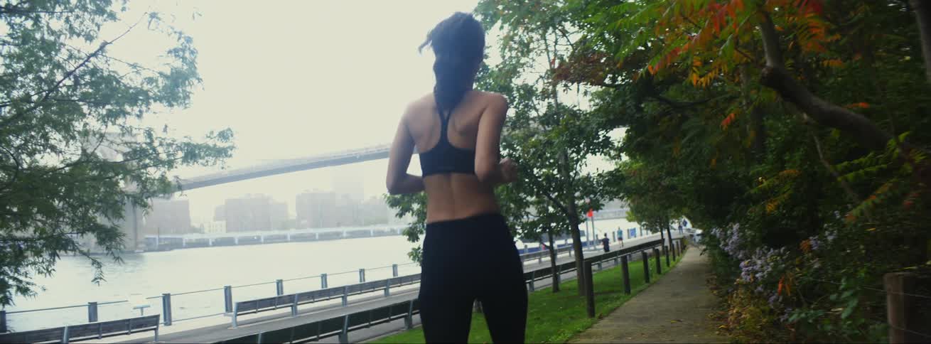 A woman jogs along a path beside a river on a foggy morning