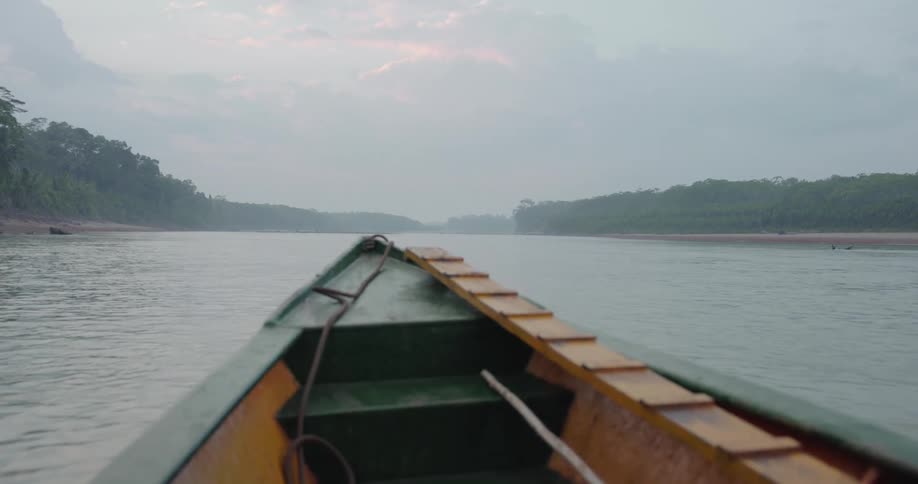 Canoe moves along river toward horizon passing misty forests