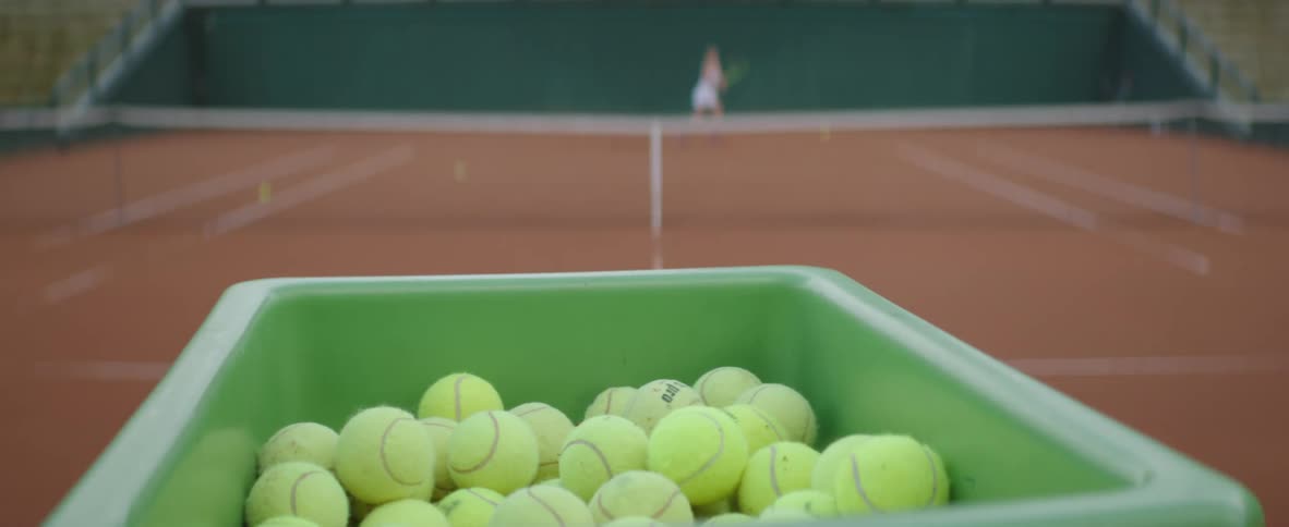 A tennis ball launcher shoots out balls to a woman playing across the court