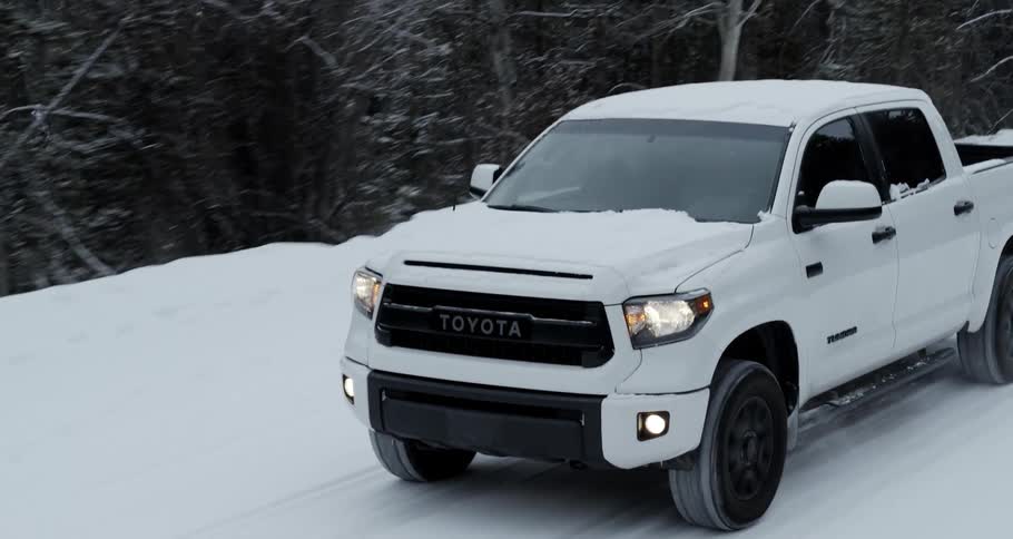 White toyota truck driving on a countryside road covered in snow near the pine tree forest in the mountain